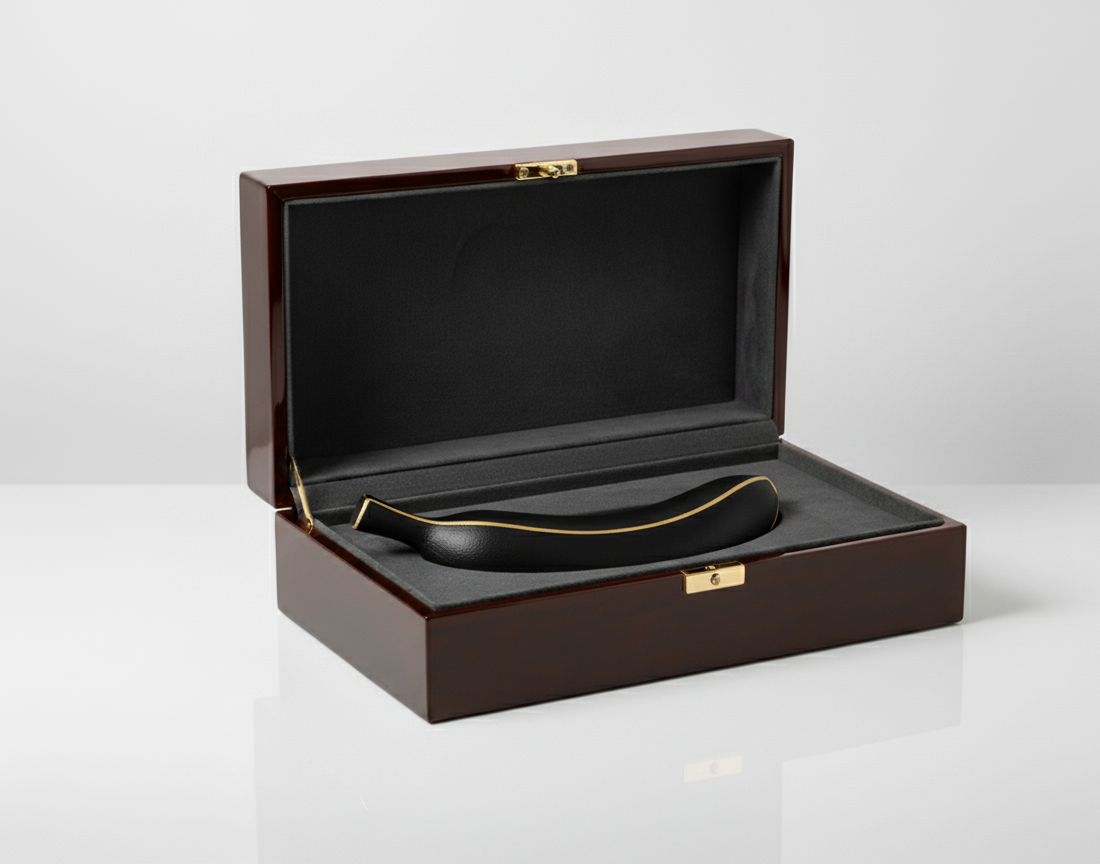 The black banana sculpture with gold detailing displayed inside a luxurious dark wooden box lined with black velvet and gold hardware.