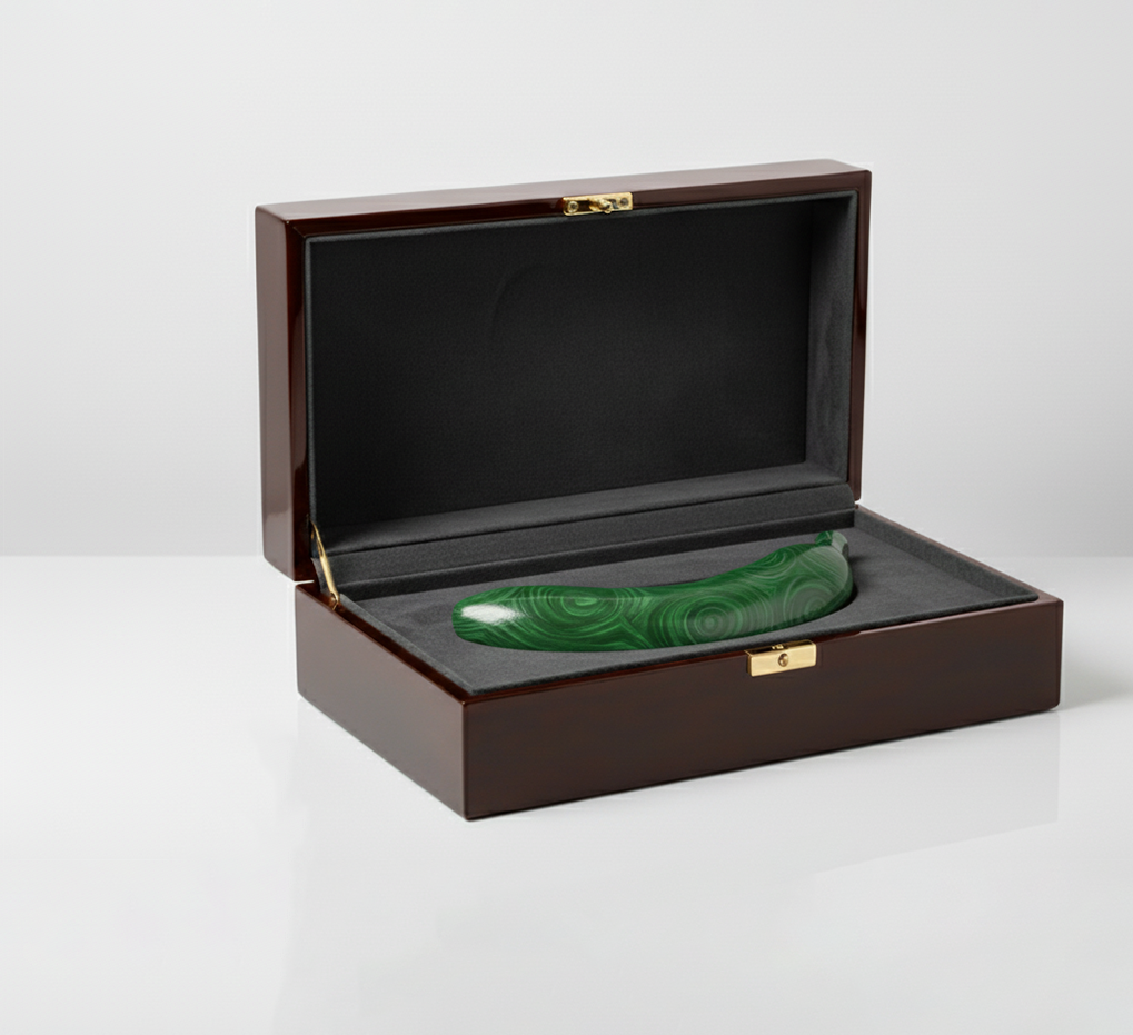 The green banana sculpture elegantly placed inside a luxurious dark wooden presentation box lined with black velvet and gold hardware, viewed in soft lighting.